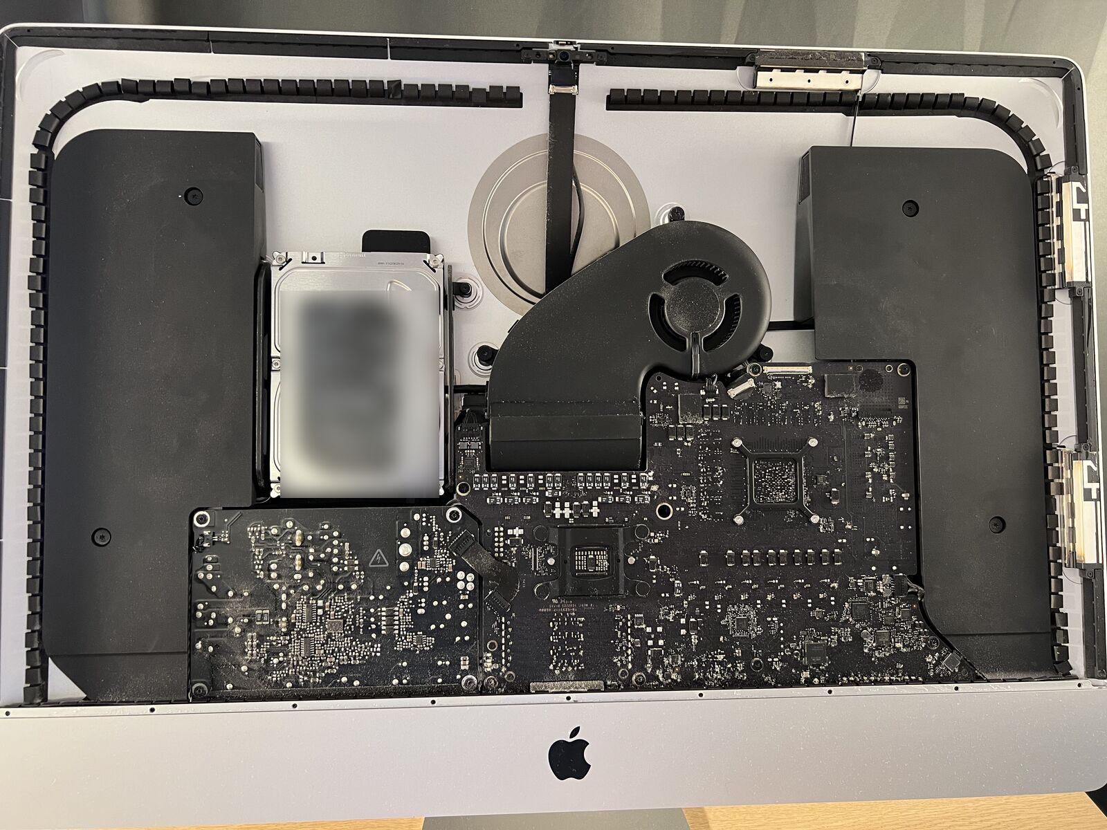 A 27-inch 5K iMac lying face up with the display panel removed: the logic board, the power supply, the fan, the hard drive and the two speakers are exposed inside the aluminium housing.