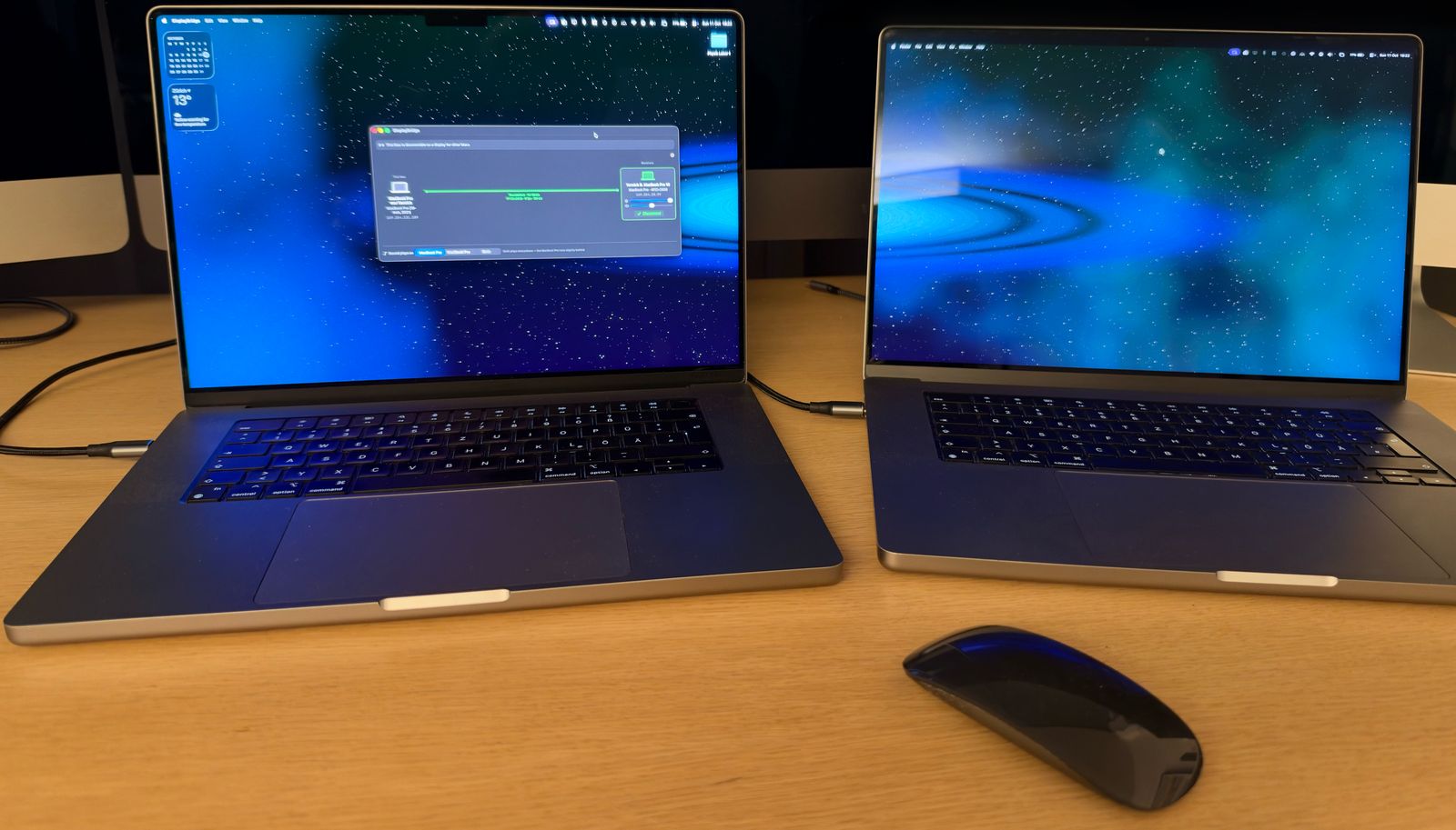 Two 16-inch MacBook Pros side by side on a desk, connected by one Thunderbolt cable. The left one shows the DisplayBridge window with a green connection line; the right one shows the extended desktop with a space wallpaper.