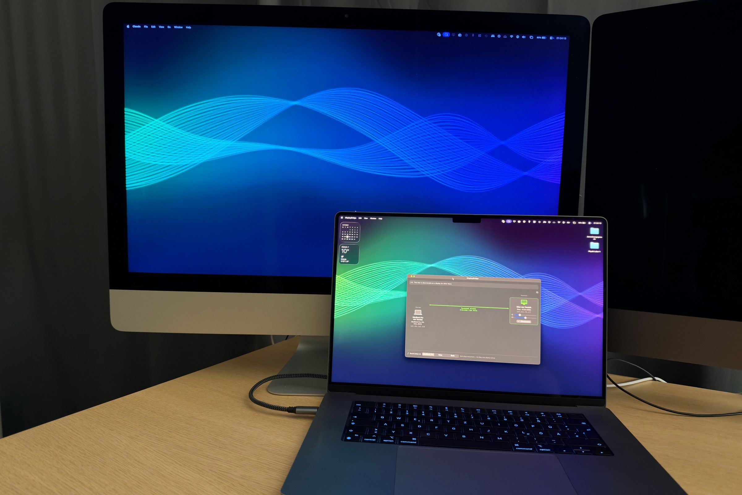 A 27-inch iMac with a blue wave wallpaper as the second display of the MacBook Pro in front of it, which shows the DisplayBridge window; one cable connects them.